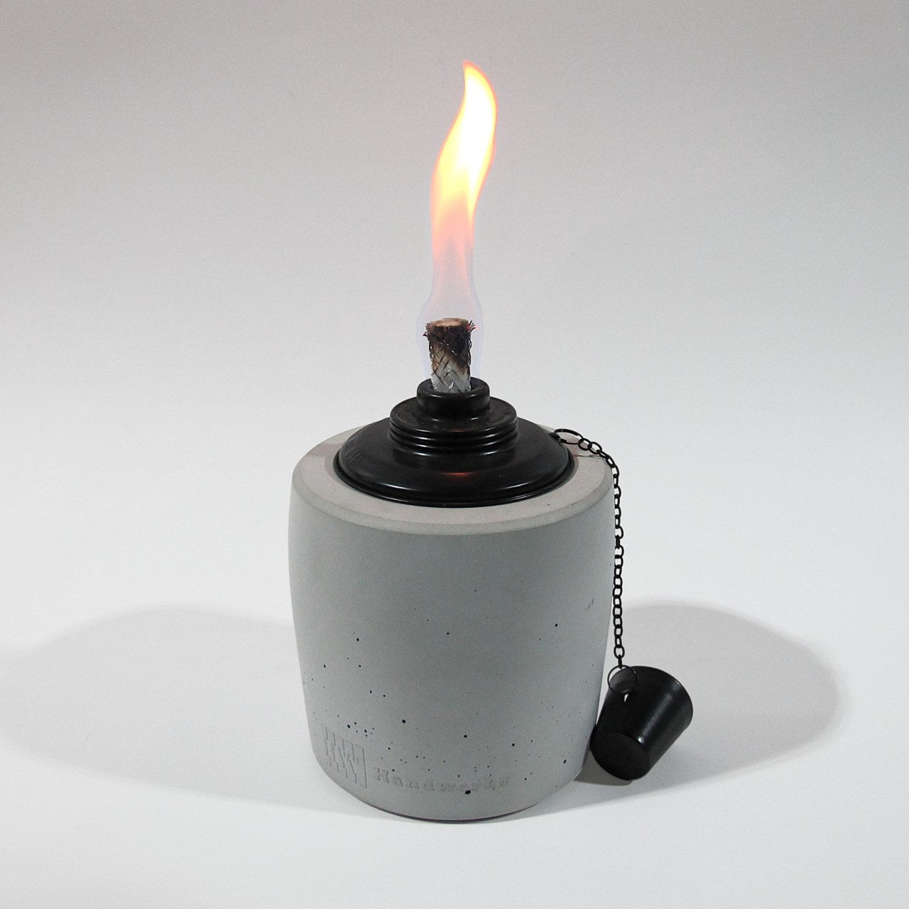 Gartenfackel in Grau mit 13cm Durchmesser und 19cm Hoch. Der schwarze Einsatz des Ölbrenners erzeugt eine schöne gleichmäßige Flame. Der Löschdeckel hängt an einer feinen Kette auf der rechten Seite herunter.